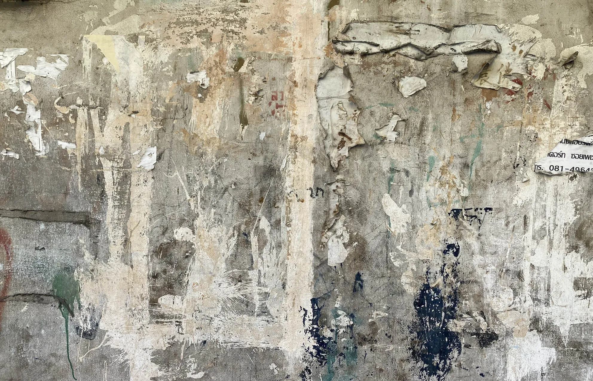 Weathered wall with peeling posters and paint splatters in grey, beige and dark blue