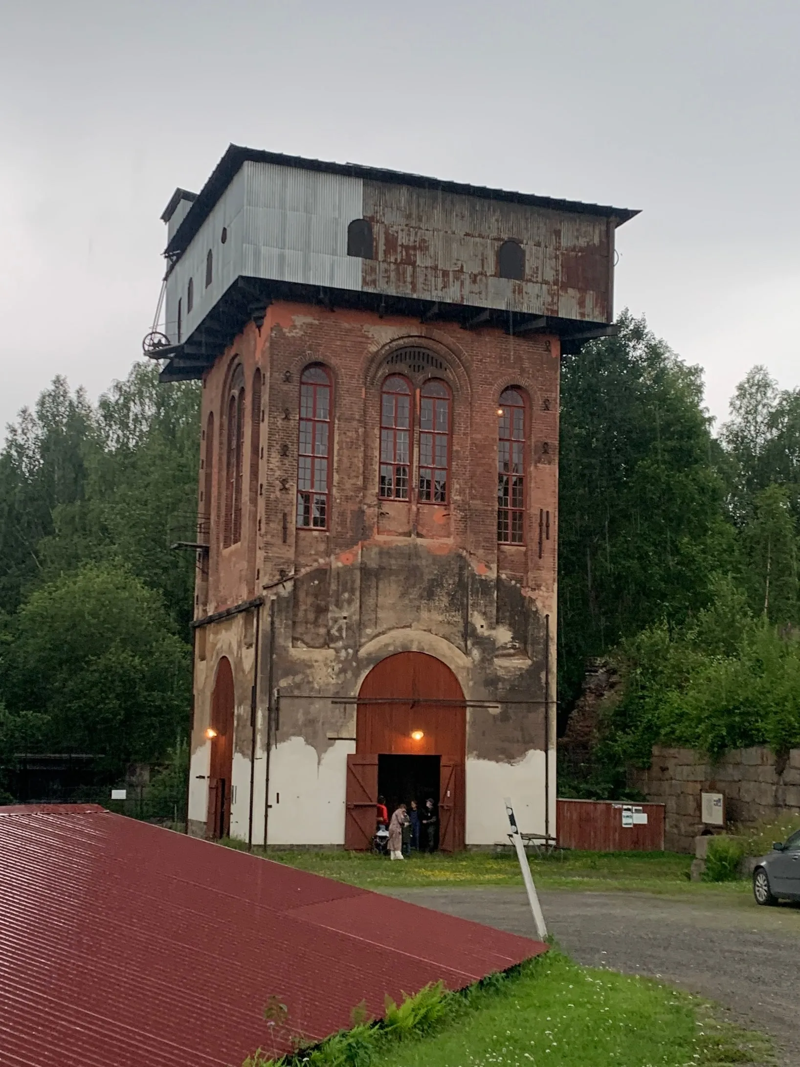 Old brick and corrugated-metal mining tower with a large arched door and visitors outside