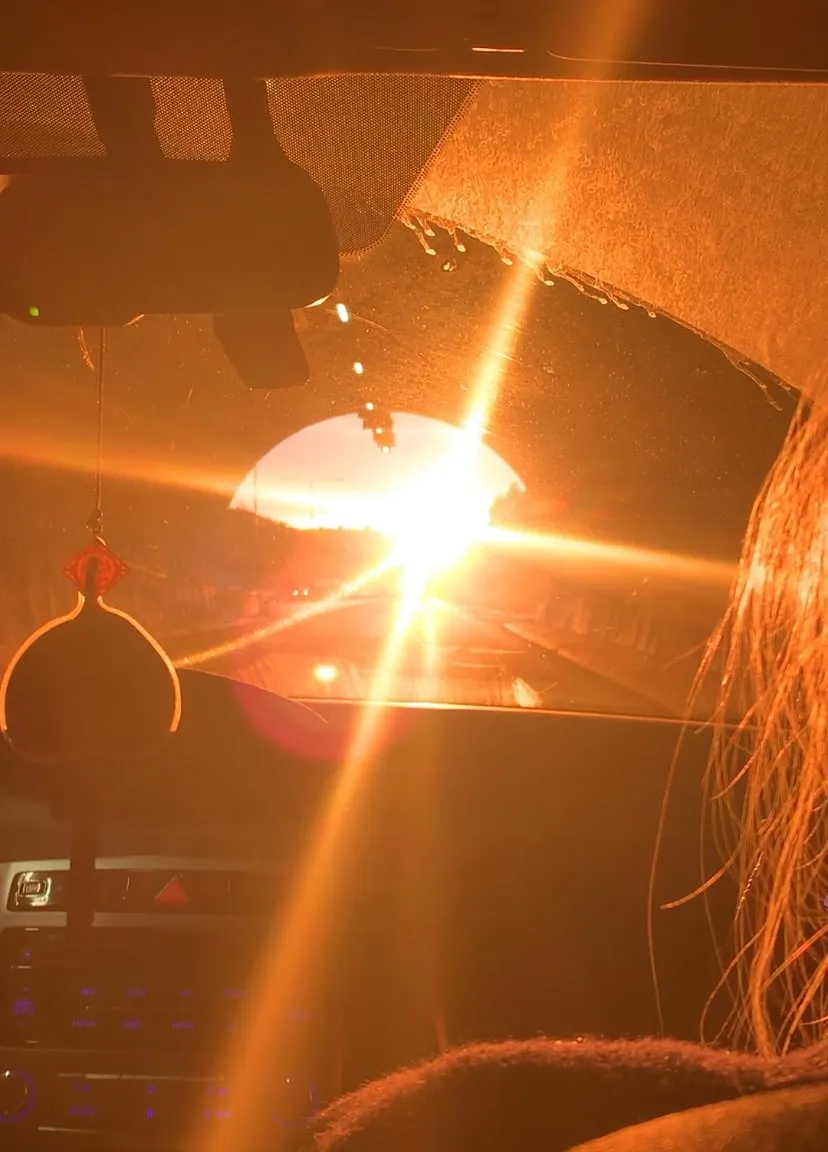 Sun flaring in a tunnel opening, seen through a car windshield with a hanging ornament and a person's hair