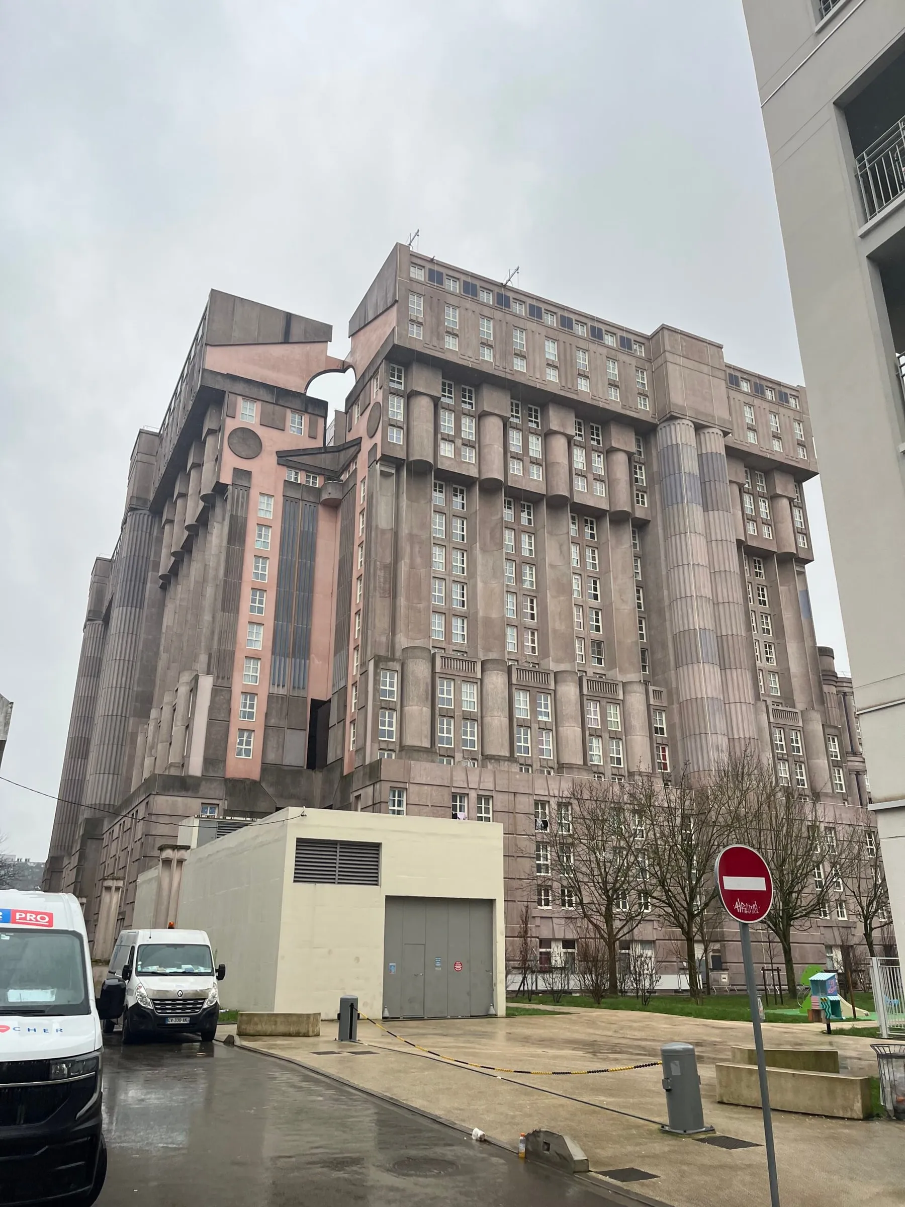 Large pink-grey postmodern housing block with columns, seen from the street on a rainy day